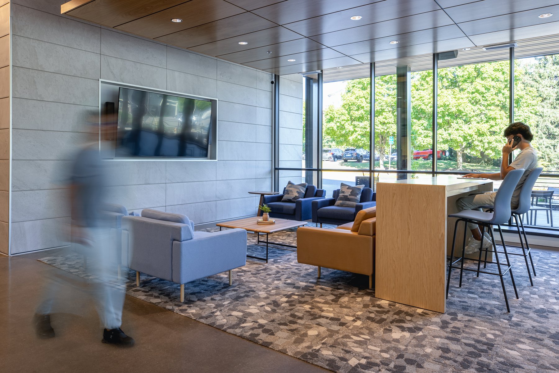 Kentucky University — lounge seating with blue and tan armchairs beside a wall-mounted TV and a bar-height table