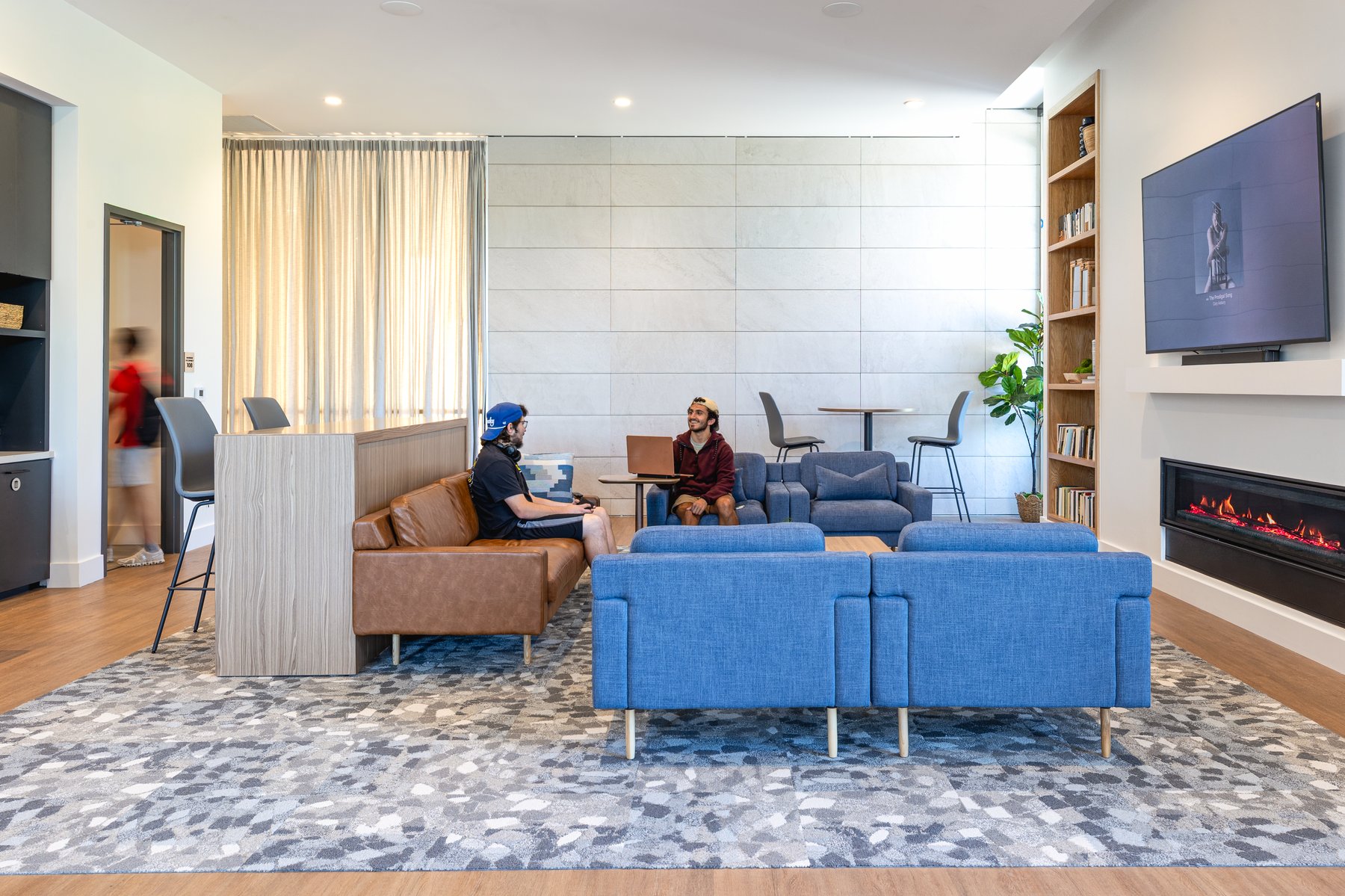 Kentucky University — fireside lounge with a brown leather sofa, blue armchairs, and a built-in bookshelf